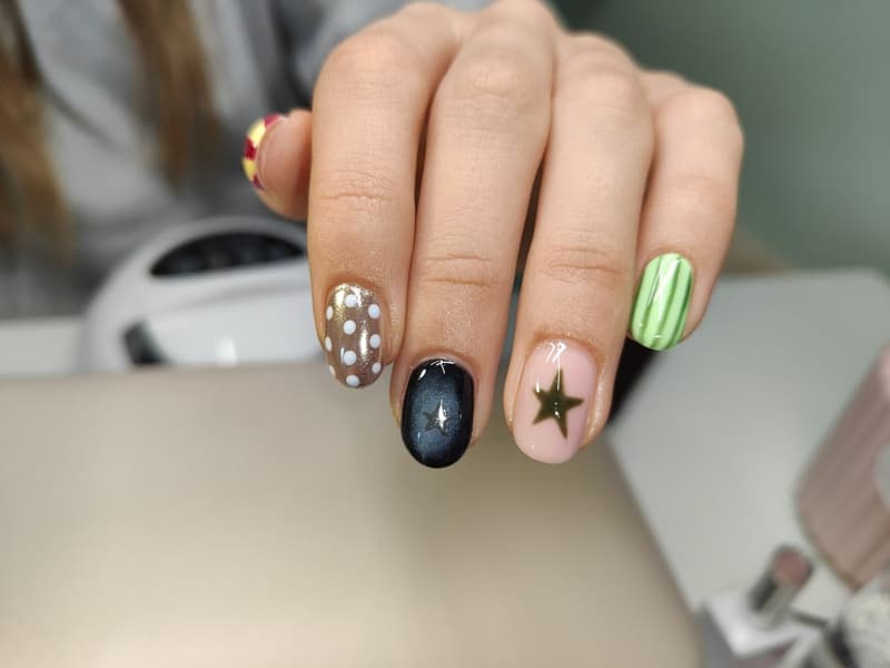 Nagels met bruine stippen, een zwarte cat eye, een gouden ster en groene strepen
