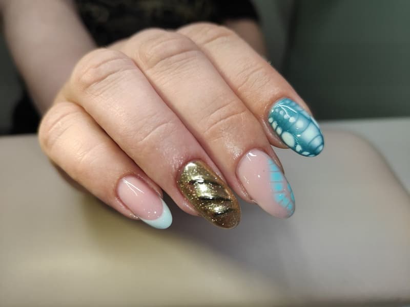 Nude nagels met een blauwe french, gouden glitter en een blauw patroon