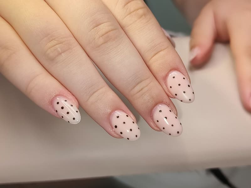 Lange amandelnagels in zacht nude met kleine zwarte stippen