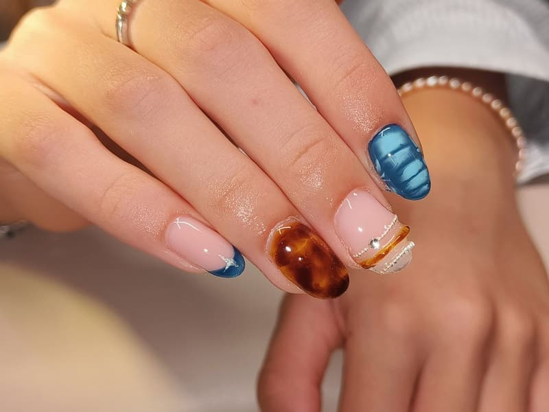 Nagels met een tortoisepatroon, een blauwe french en blauwe glansstrepen
