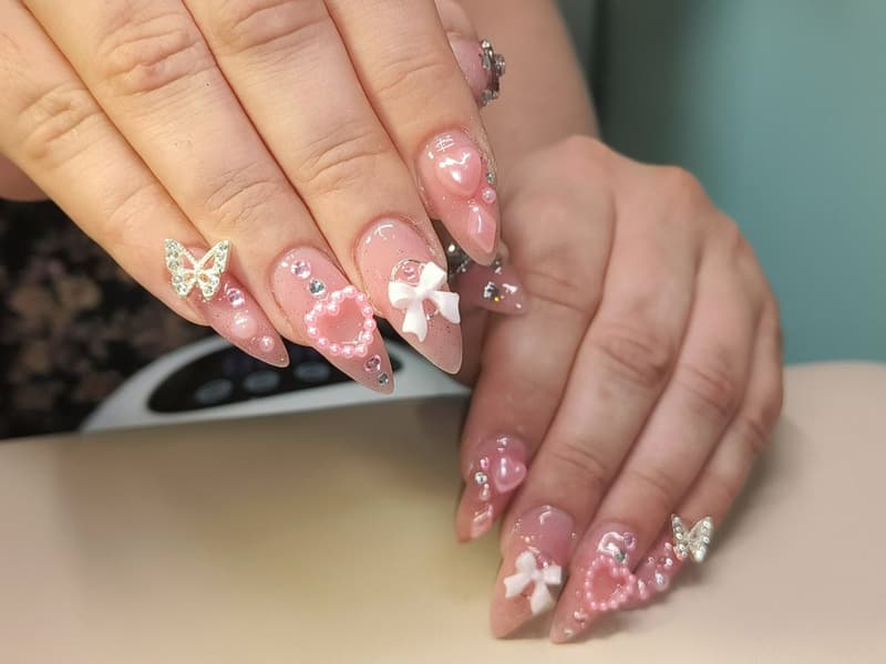 Lange roze stilettonagels met 3D-strikjes, hartjes, een vlinder en steentjes